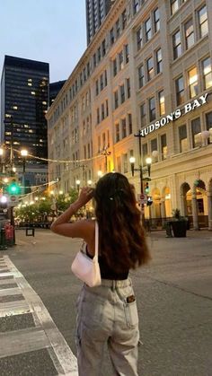 a woman standing in the middle of a street at night with her back to the camera