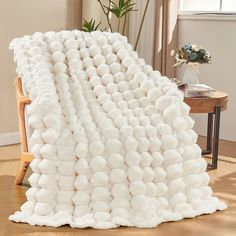 a large white blanket sitting on top of a wooden floor next to a chair and table