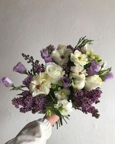 a hand holding a bouquet of white and purple flowers