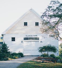 a large white barn with trees and bushes around it