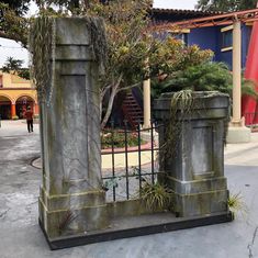 an iron gate with plants growing out of it in the middle of a cement courtyard