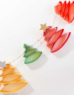 paper christmas tree decorations hanging from string on white wall with star decoration above them,