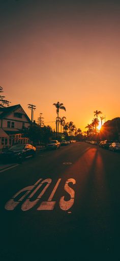 the sun is setting behind palm trees and houses on the side of an empty street