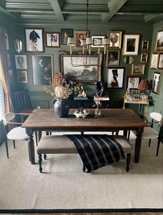 a dining room with green walls and pictures hanging on the wall, along with an upholstered bench