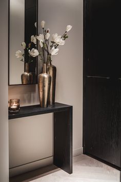 two vases with flowers are on a table in front of a mirror and candle