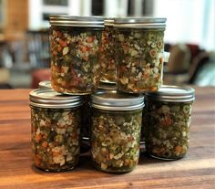 six jars filled with pickles sitting on top of a wooden table