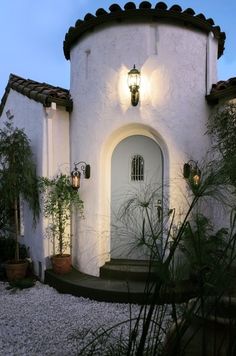 a white house with plants and lights on the front door is lit up at night