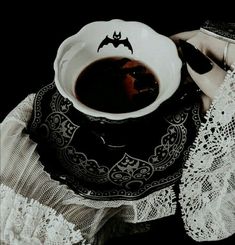 a tea cup and saucer on a lace doily with a bat motif in the middle