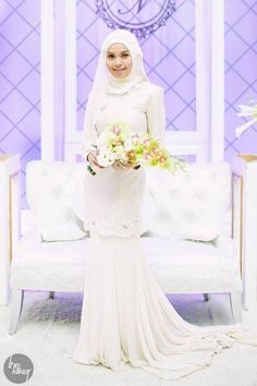 a woman standing in front of a white couch holding a flower bouquet and wearing a hijab