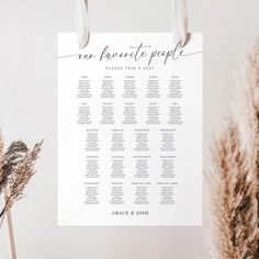 a white wedding seating plan hanging on a wall next to some dried plants and flowers