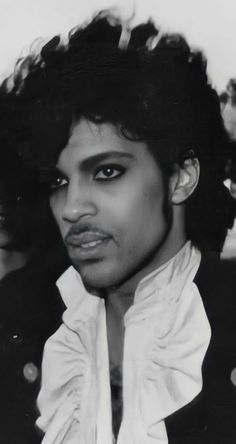 a black and white photo of a man with curly hair wearing a jacket, looking at the camera