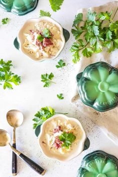 two bowls filled with soup and garnished with parsley on the side next to spoons