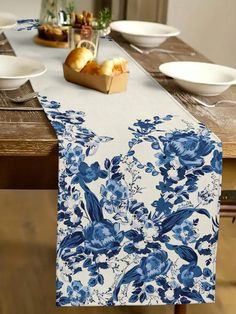 a blue and white floral table runner on top of a wooden table with bowls of food in the background