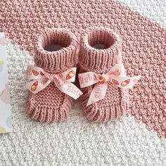 a pair of pink knitted baby booties sitting on top of a white and pink blanket