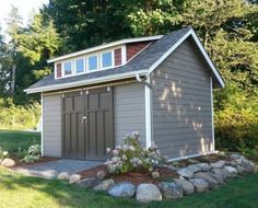 a small shed sitting in the middle of a yard with rocks and flowers around it