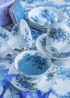 blue and white porcelain dishes with flowers on them are sitting on a tablecloth next to an open book