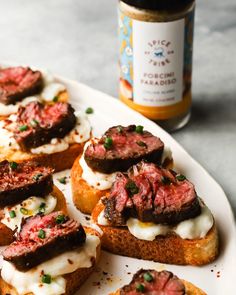 several pieces of bread topped with meat and cream on a plate next to a jar of mustard