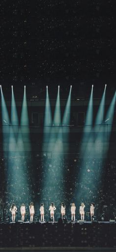 a group of people standing on top of a stage in front of spotlights with their backs turned