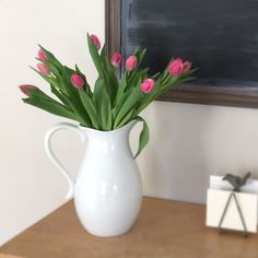 a white vase filled with pink flowers on top of a table