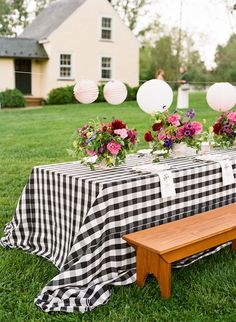 a picnic table set up in the grass with flowers and balloons hanging from the ceiling