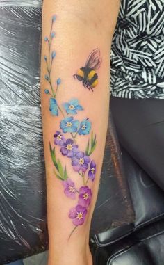 a woman's arm with flowers and a bee on it, while she is sitting down