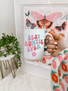 a woman holding a coffee mug with the words best aunt ever in pink and green