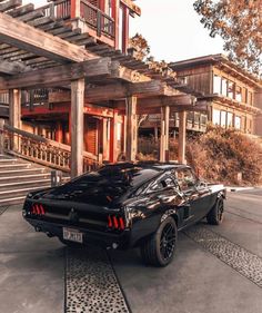 a black muscle car parked in front of a wooden building with stairs and balconies