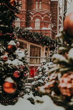 christmas trees are decorated with red and gold ornaments in front of an old brick building