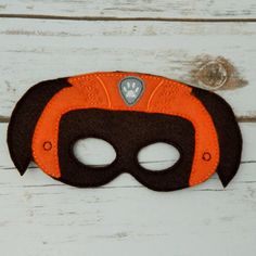 an orange and black mask on top of a white wooden table with wood planks