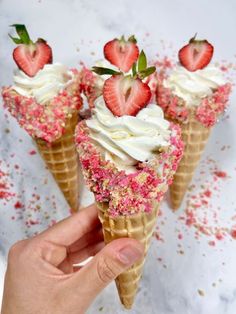 three ice cream cones with strawberries and sprinkles on top are being held up