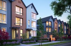 a row of multi - family houses at dusk with trees and flowers in the foreground