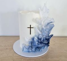 a white cake with blue ruffles and a cross on top