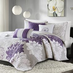 a bed with purple and white comforters on top of it in a room next to a window