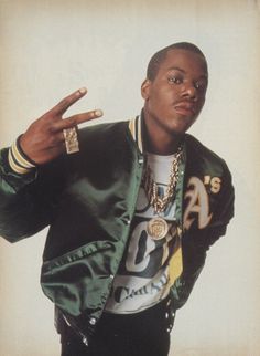 a man in a green jacket making the peace sign with his hand while standing against a white background