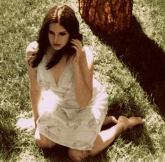 a woman sitting in the grass next to a tree