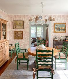 the dining room table is surrounded by green chairs and matching wallpaper with pictures on the walls