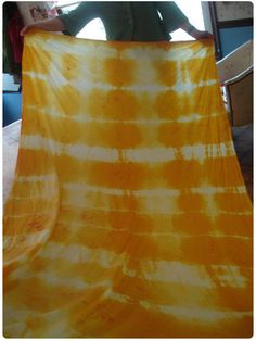 a person holding up a yellow and white tie - dyed blanket