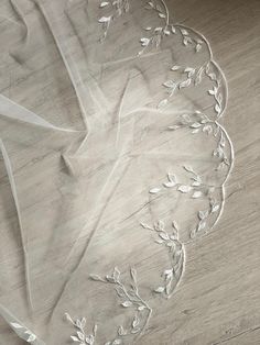 an embroidered white cloth with leaves and vines on the bottom is laying on a wooden floor