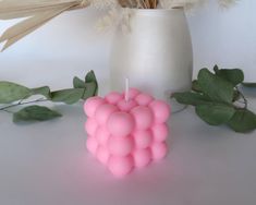 a pink candle sitting on top of a table next to some leaves and flowers in a vase