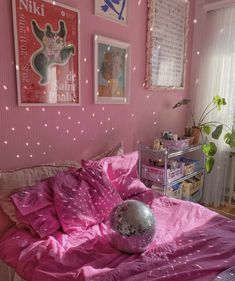 a bedroom with pink walls and pictures on the wall above the bed, along with a disco ball