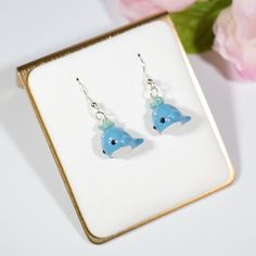 a pair of earrings sitting on top of a white table next to a pink flower