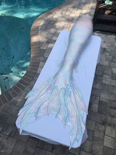 a woman laying on top of a white sheet next to a swimming pool covered in mermaid tails