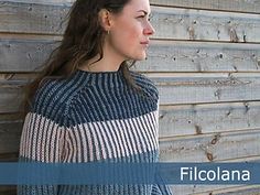 a woman standing in front of a wooden wall wearing a blue and white sweater with stripes