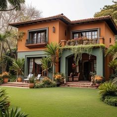 an orange house with lots of plants and trees in front of it, surrounded by greenery