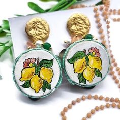 a pair of earrings with lemons painted on the front and back, sitting next to a bead necklace