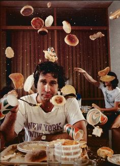 a man sitting at a table with lots of food flying over his head and hands