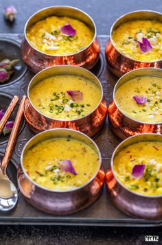 there are many bowls of soup on the tray with utensils and spoons