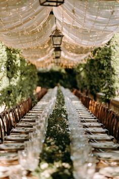 the long table is set with clear glassware and place settings for guests to sit at