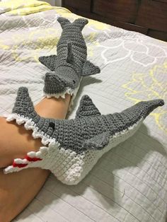 two crocheted shark gloves laying on top of a person's leg in bed