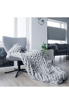 a large chunky blanket sitting on top of a chair next to a plant in a living room